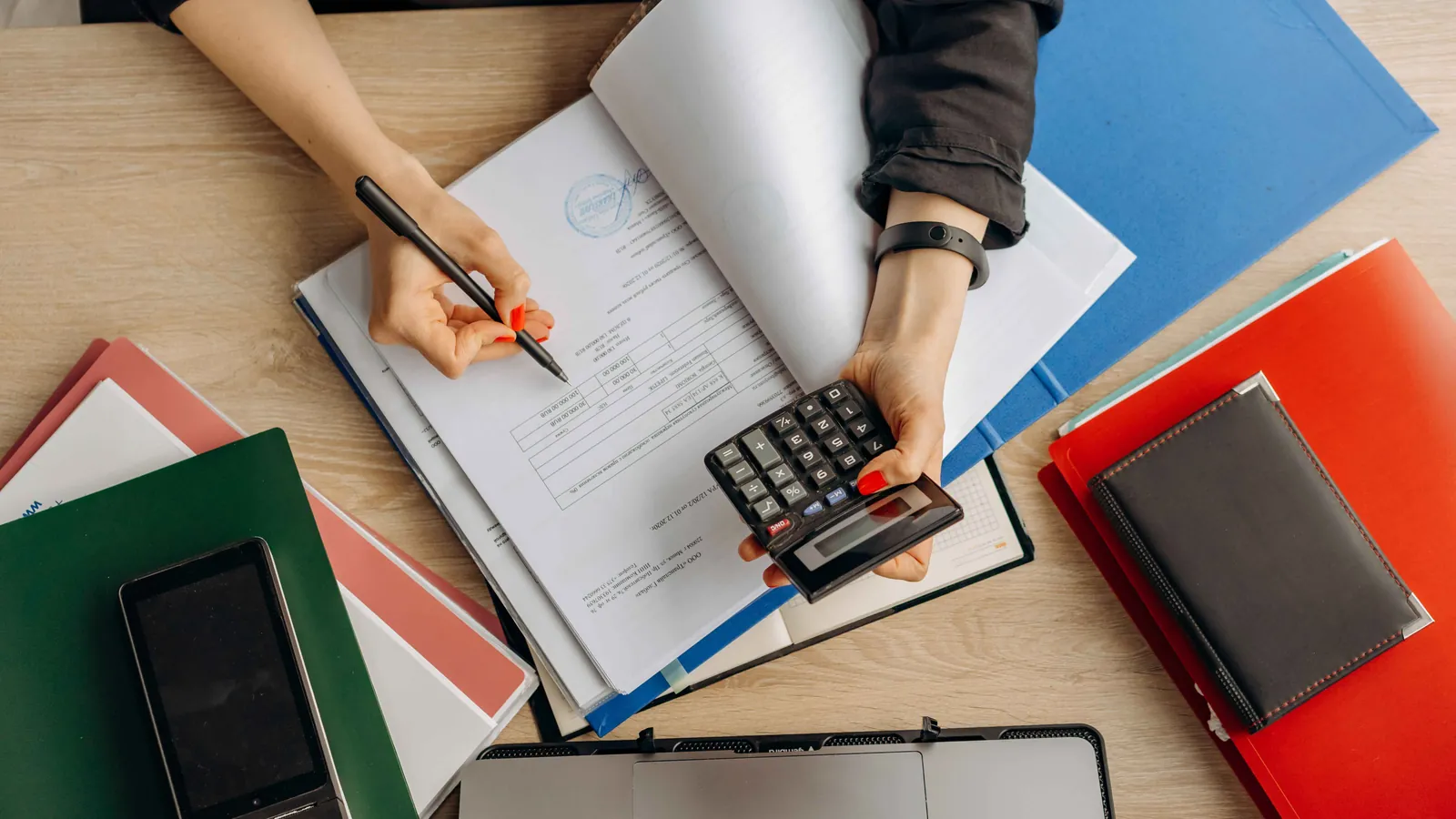 Person reviewing paperwork with a pen and calculator at a desk