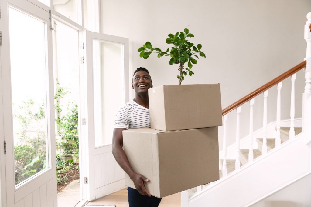 man holding plant and boxes in home and moving