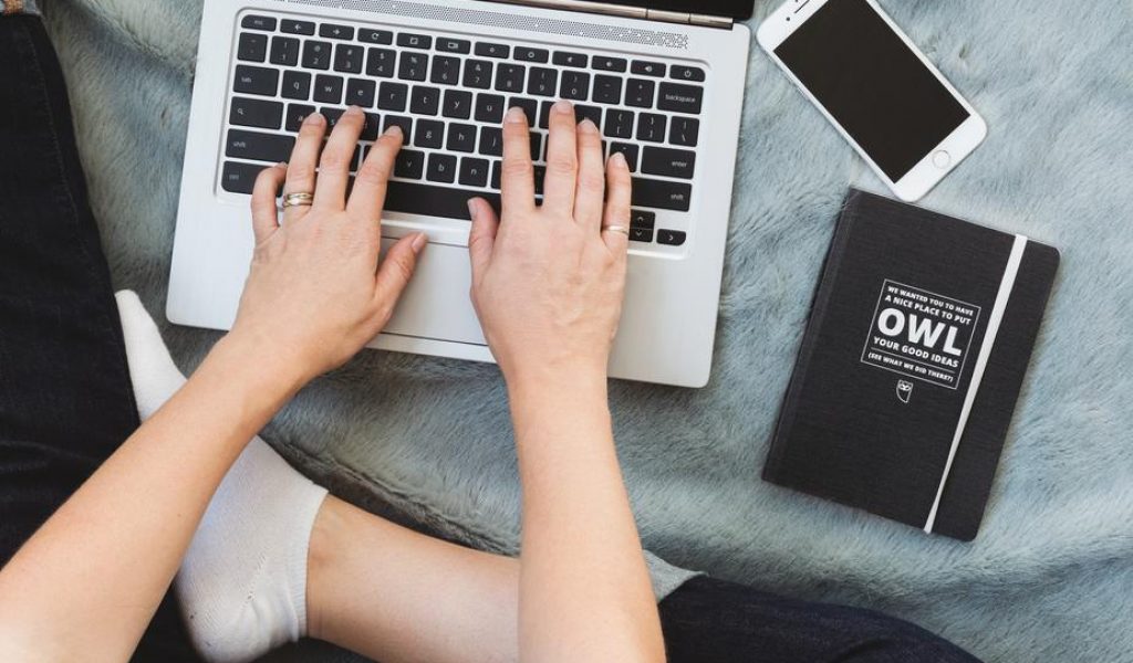 person-working-on-laptop-with-phone-and-notebook-beside